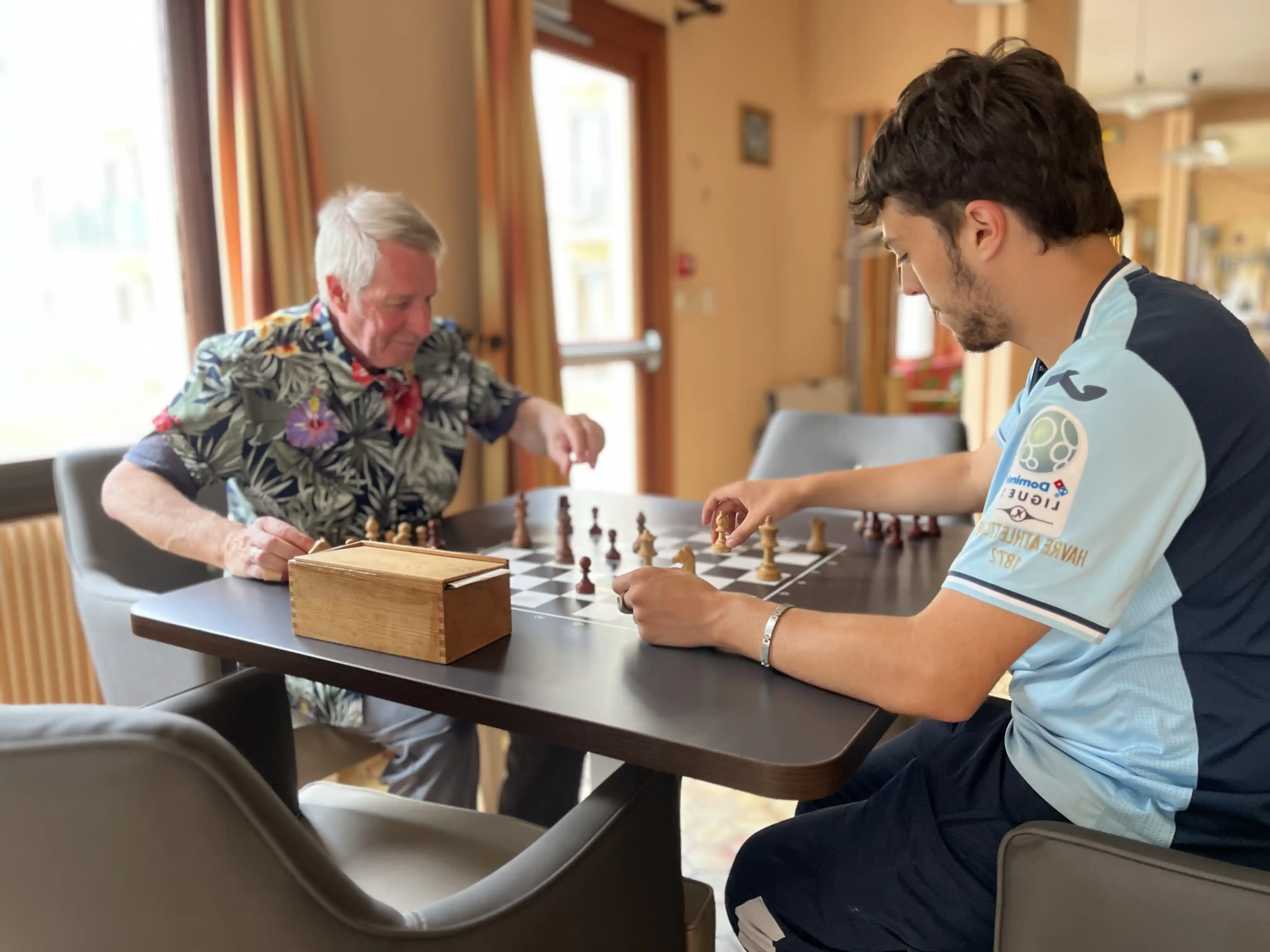Une personne agée et un jeune adulte jouant aux échecs sur une table