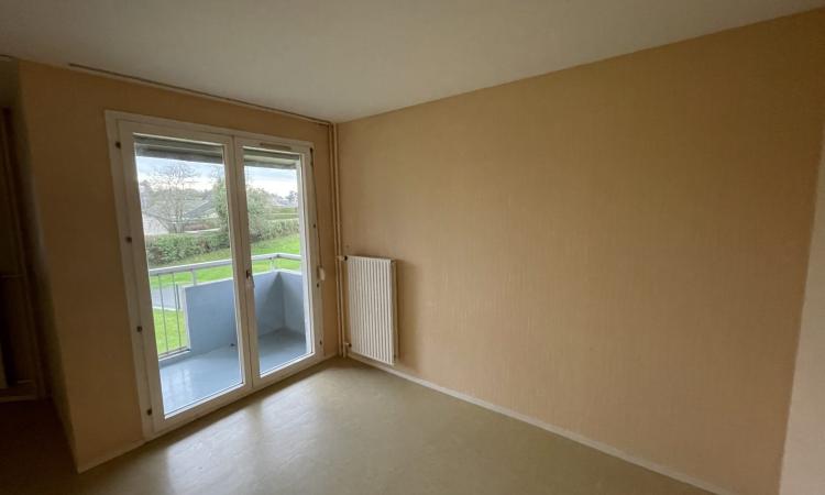 Pièce avec murs orange et porte-fenêtre avec volet roulant donnant sur un balcon , radiateur mural à droite de la fenêtre.
