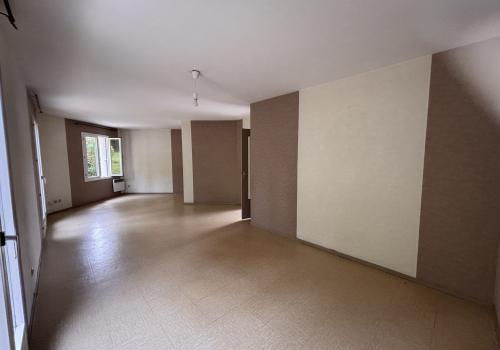 Pièce de vie avec murs couleur taupe et beige, sol beige, 2 portes fenêtres à 2 battants et une fenêtre simple à 2 battants. Un radiateur mural est présent sous la fenêtre simple.